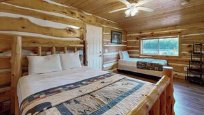 A log cabin bedroom with a bed, a bench, a ceiling fan, and a window. - Cozy Cabin located on the Turtle Flambeau Flowage, great for all seasons! (Mercer)