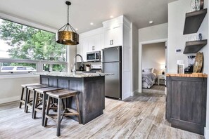 Una cocina moderna con una isla central, taburetes de bar, electrodomésticos de acero inoxidable y vistas al exterior.