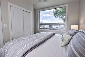Un dormitorio con cama, ventana con vistas al exterior y puerta.