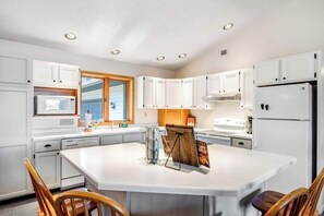 A kitchen with white cabinets, a central island, a microwave, a refrigerator, and wooden chairs. - Lakefront Lodge w/ Firepit, Private Dock, and Kayaks - Dogs Welcome (Manitowish Waters)