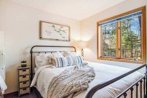 Een slaapkamer met een bed, een nachtkastje met een lamp, een inlijsting kaart aan de muur, en een raam met uitzicht op bomen.
