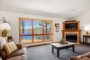 A living room with a large window, fireplace, and television. - Lakefront Lodge w/ Firepit, Private Dock, and Kayaks - Dogs Welcome (Manitowish Waters)