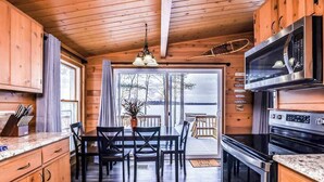 A wooden interior with a kitchen, dining area, and a view through a glass door. - Fantastic lakefront home with fireplace, fast WiFi, washer/dryer & dog-friendly (Manitowish Waters)