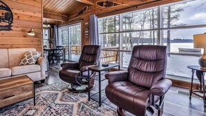 A cabin interior with a wooden ceiling, leather chairs, a sofa, and large windows overlooking a lake. - Fantastic lakefront home with fireplace, fast WiFi, washer/dryer & dog-friendly (Manitowish Waters)