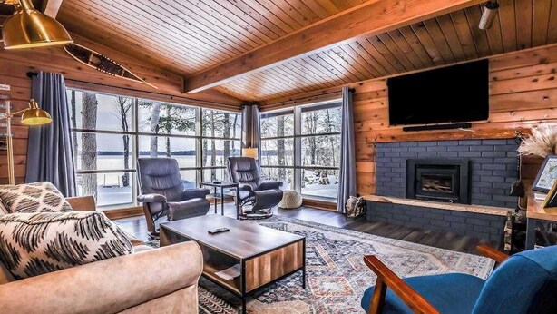 A cozy living room with a fireplace, large windows, and a television mounted on the wall. - Fantastic lakefront home with fireplace, fast WiFi, washer/dryer & dog-friendly (Manitowish Waters)