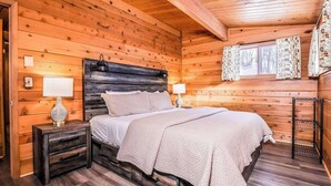 A wooden cabin bedroom with a bed, nightstands, and a window with curtains. - Fantastic lakefront home with fireplace, fast WiFi, washer/dryer & dog-friendly (Manitowish Waters)
