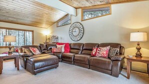 Ein Wohnzimmer mit einem braunen Ledersofa, einer großen Wanduhr und einer Holzbalkendecke.
