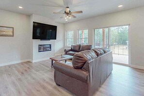 A spacious living room with a large leather sofa, a flat-screen TV mounted on the wall, and a ceiling fan. - Modern Northwoods Townhouse near lakes, trails & town‚Äîperfect for adventures! (Eagle River)