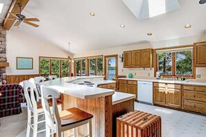 Eine moderne Küche mit Holzschränken, einer großen Kochinsel und einem Essbereich mit weißen Stühlen.