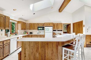 Eine moderne Küche mit Holzausstattung, einer zentralen Kochinsel und einem Essbereich mit weißen Stühlen.