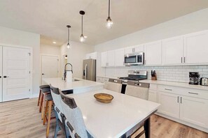 A modern kitchen with white cabinets, a central island, pendant lighting, and a stainless steel refrigerator.