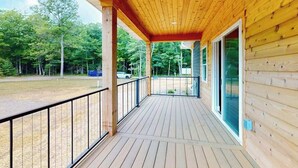 Eine Holzterrasse mit Geländer, eine überdachte Veranda und Blick auf einen bewaldeten Bereich.