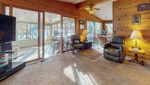 A spacious living room with a television, leather chairs, a coffee table, and a ceiling fan. - Lakefront home with, dock, grill, sunporch, WIFI, W/D near Downtown (Eagle River)