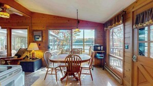A wooden interior with a dining table, chairs, a lamp, and a view of the outdoors. - Lakefront home with, dock, grill, sunporch, WIFI, W/D near Downtown (Eagle River)