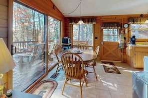 Una cabaña de madera con comedor, ventanas grandes y vistas al bosque.