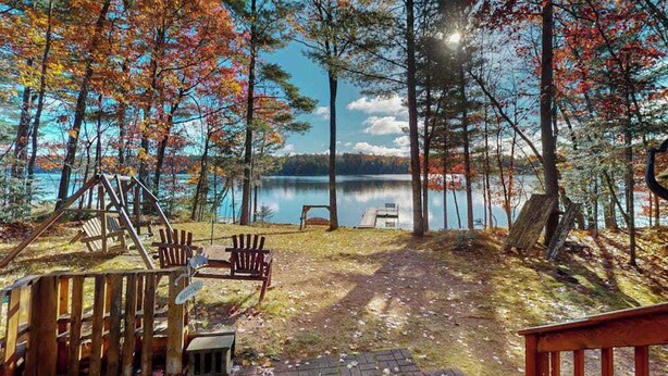 A lakeside cabin with a wooden deck, a swing set, and a bench. - Lakefront home with, dock, grill, sunporch, WIFI, W/D near Downtown (Eagle River)