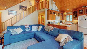 Una sala de estar moderna con un sofá seccional azul, una escalera de madera y una zona de cocina.