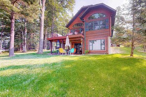 A two-story log cabin with a covered patio and outdoor seating area. - Serene Lakefront Home w/ Wifi, dock, kayaks, gas grill, fire pit & more (Eagle River)