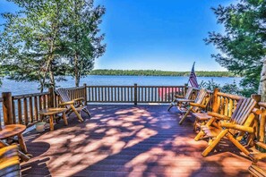 Eine Holzterrasse mit Adirondack-Stühlen und Blick auf einen See.