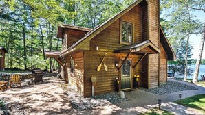 A wooden cabin with a covered patio, a grill, and a door with a window. - Lakefront retreat with two full kitchens, fireplaces, washer/dryer, & two docks (Eagle River)