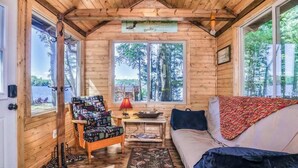 A cabin interior with a wooden ceiling, a sofa, a chair, a window, and a sign above the window. - Lakefront retreat with two full kitchens, fireplaces, washer/dryer, & two docks (Eagle River)