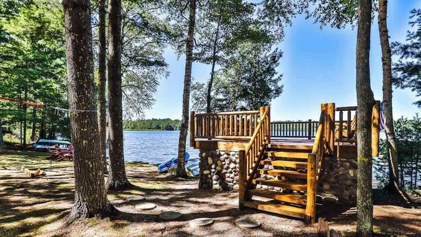 A wooden deck with a stone base, surrounded by trees, leading to a dock by a lake. - Lakefront retreat with two full kitchens, fireplaces, washer/dryer, & two docks (Eagle River)