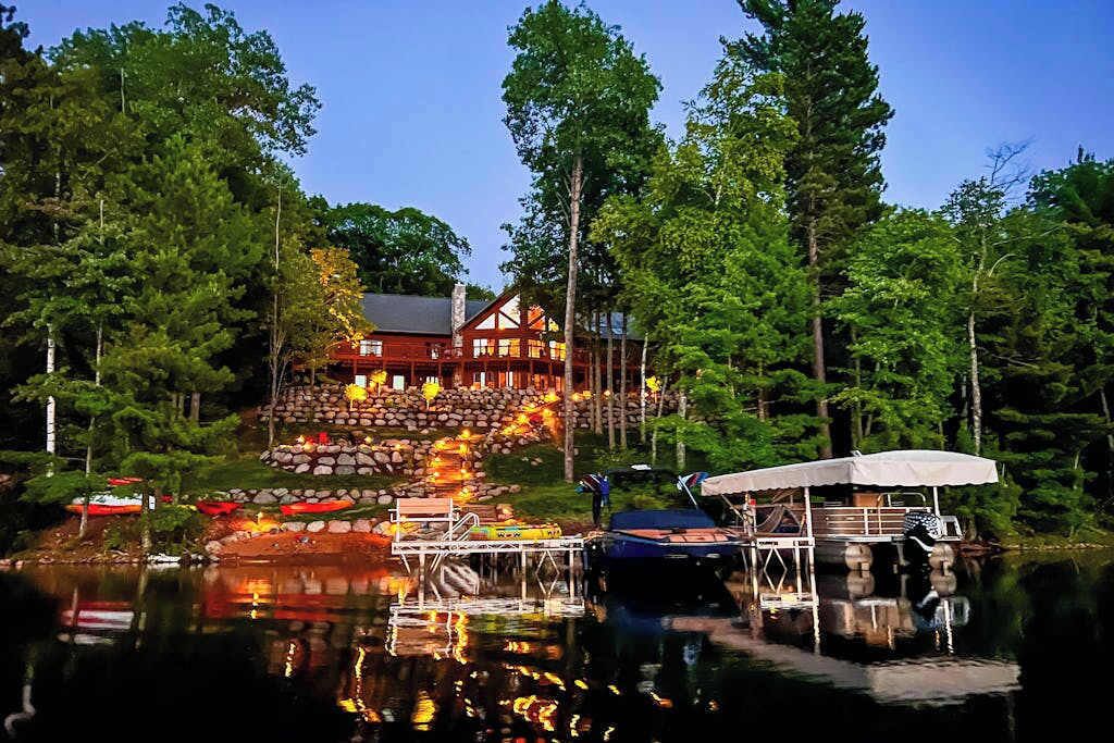 A lodge with a dock, a stone staircase, and a large wooden building surrounded by trees.