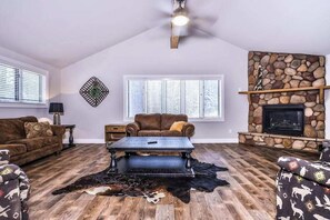 A living room with a stone fireplace, a ceiling fan, and a large window with blinds. - Updated, tree-lined home on the snowmobile trail with gas fireplace & firepit (Manitowish Waters)