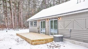 Eine Holzhütte mit einer Holzterrasse, großen Fenstern und einem mit Schnee bedeckten Dach.