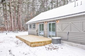 A cabin with a wooden deck, large windows, and a snow-covered roof. - Updated, tree-lined home on the snowmobile trail with gas fireplace & firepit (Manitowish Waters)