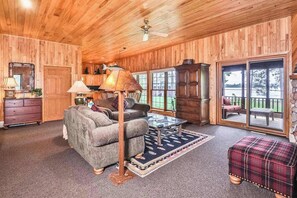 A wooden-paneled room with a sofa, a lamp, a cabinet, and a large window.