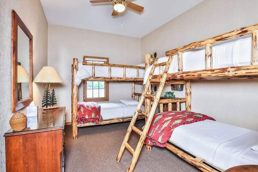 A room with bunk beds, a ceiling fan, a lamp, a small table with a decorative item, and a window.