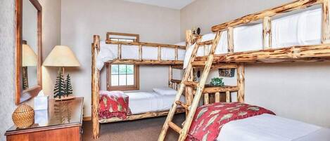 A room with bunk beds, a ceiling fan, a lamp, a small table with a decorative item, and a window.