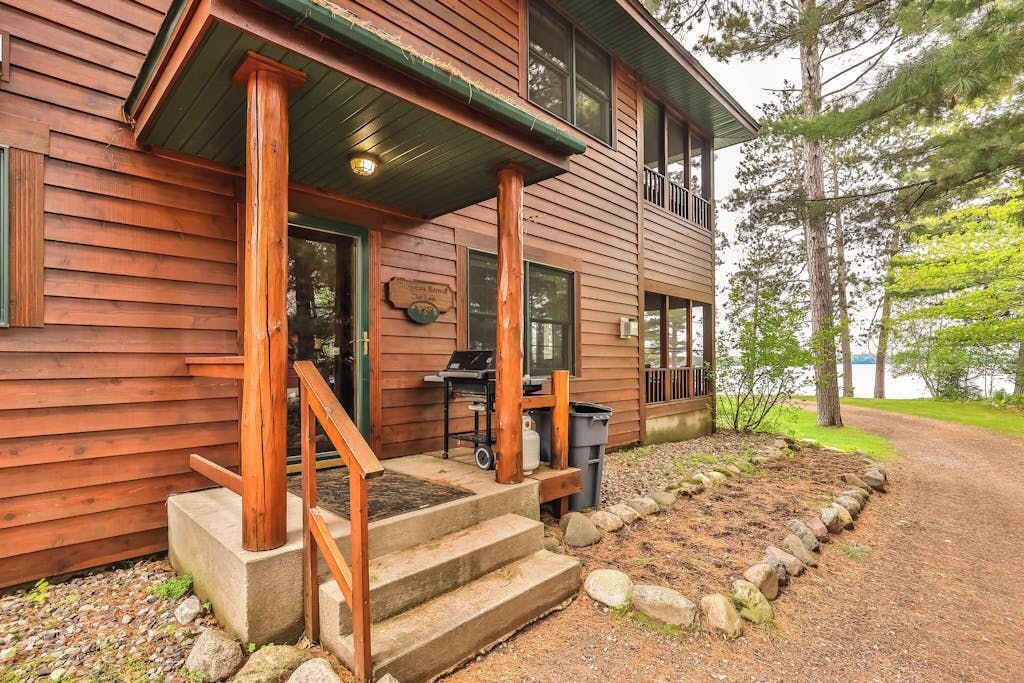 Une cabane en bois avec une véranda, des marches et un barbecue à l’extérieur.