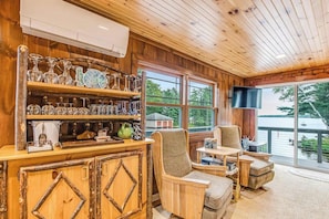 Un intérieur en bois avec un espace bar, des chaises et de grandes fenêtres donnant sur une étendue d’eau.