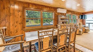 Une pièce aux murs lambrés, comprenant une table à manger et des chaises, une bibliothèque et un téléviseur.