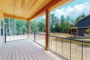 Ett trädäck med ett metallräcke, med utsikt över ett skogsområde och en byggnad.