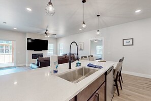 Una cocina moderna con una isla grande, pileta de acero inoxidable, lámparas colgantes y un ventilador de techo.