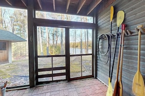A covered porch with a wooden floor, a glass door leading outside, and several paddles and a canoe on the wall.