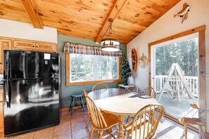A kitchen with a black refrigerator, wooden dining table, and chairs, a window with a plaid curtain, and a deck with a wooden railing. - Spacious lakefront home with pier views, canoe, and fire pit - family-friendly (Land O'Lakes)