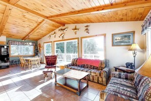 A cozy living room with wooden ceiling beams, a dining area with a table and chairs, and a sofa with a red throw. - Spacious lakefront home with pier views, canoe, and fire pit - family-friendly (Land O'Lakes)