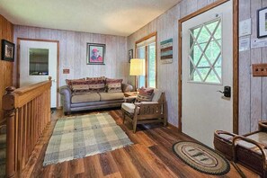 Una habitación acogedora con pisos de madera, un sofá, una silla, una lámpara y una puerta con ventanal.