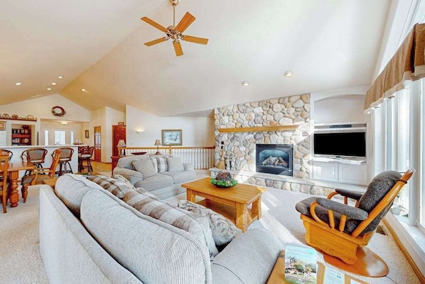 A living room with a stone fireplace, a television, and a ceiling fan.