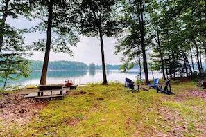Camping junto al lago con mesas de picnic, una canoa y sillas Adirondack.