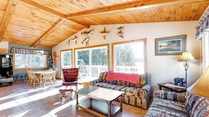 Eine Holzbalkendecke, ein Essbereich mit Stühlen und Tisch, ein Sofa, eine Lampe und ein gerahmtes Bild an der Wand.
