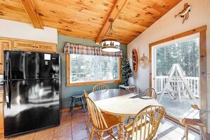 A kitchen with a black refrigerator, wooden dining table, and chairs, a window with a view of trees, and a wooden ceiling. - Beautiful home on High Lake w/private pier, large deck & canoes (Land O'Lakes)