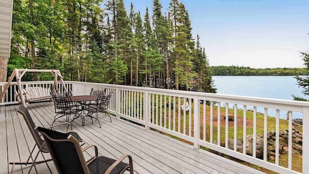 Eine Terrasse mit Gartenmöbeln, die auf einen See blickt, umgeben von Bäumen.