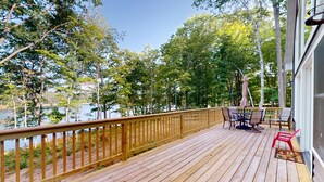 A wooden deck with a table and chairs, overlooking a body of water and surrounded by trees. - Lakefront Sunrise Lodge: fireplace, deck views, kayaks, pier & firepit (Rhinelander)