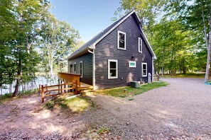 A two-story cabin with a wooden deck and a gravel driveway.