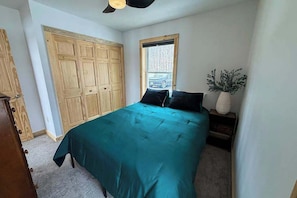 A bedroom with a bed, a window, a wooden wardrobe, and a small table with a plant.